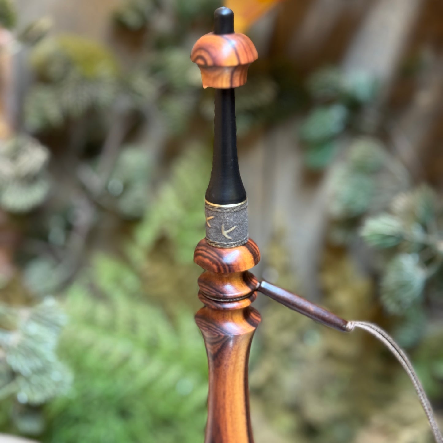 This caramel rosewood turkey trumpet as a dark buffalo horn mouth piece. The custom engraved collar shows brassy turkey foot prints and below it on the wood flute, a beaded lanyard.