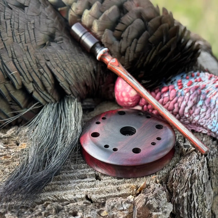jacaranda laminate custom striker and red rosy toned madagascar rosewood turkey pot call resting next to a double bearded turkey on a tree stump after a hunt