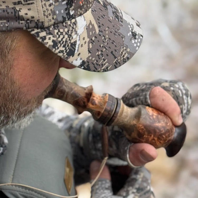 Hunter in camo hat and gloves plays a custom whitetail grunt call made of premium weru burl wood and gabon ebony wood