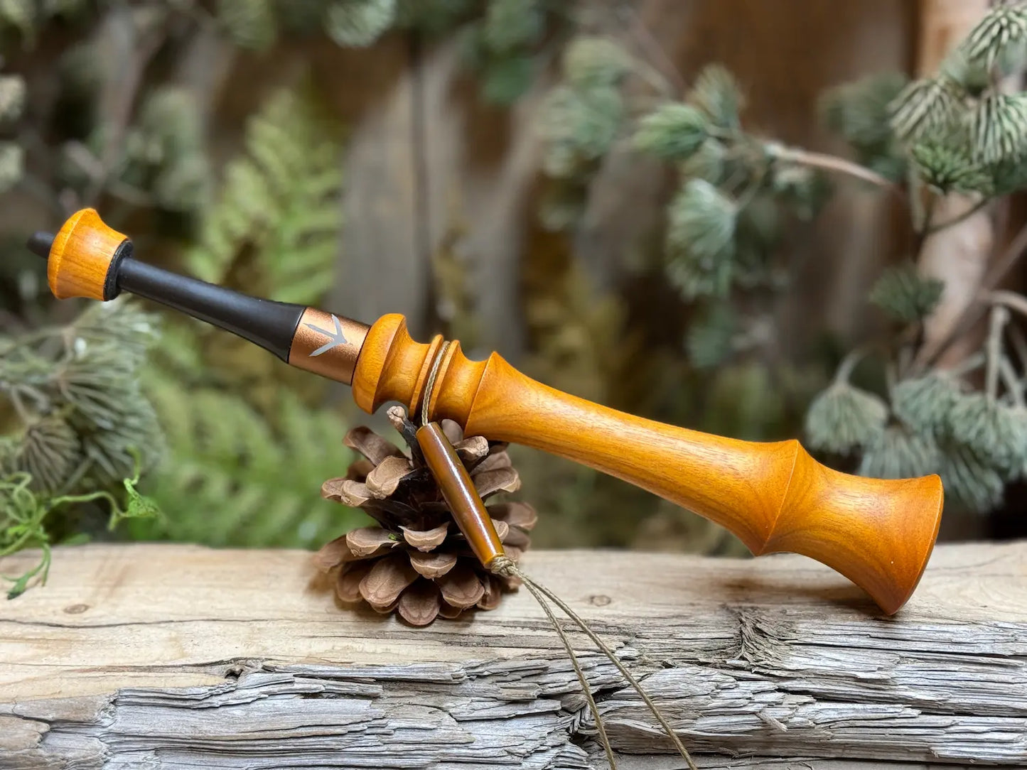 Golden yellow argentine osage wood turkey trumpet with a bronze ferrule custom laser engraved with a turkey foot imprint. The delrin and wood mouthpiece are well crafted and a custom lanyard loop hangs from the middle.