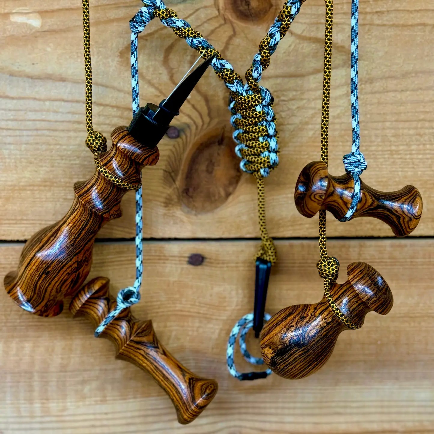 Bocote Predator Call Set with rabbit squealer, coyote howler, fawn distress bleat, and rodent squeaker hanging from a custom made lanyard woven with aqua blue and gold and black cords