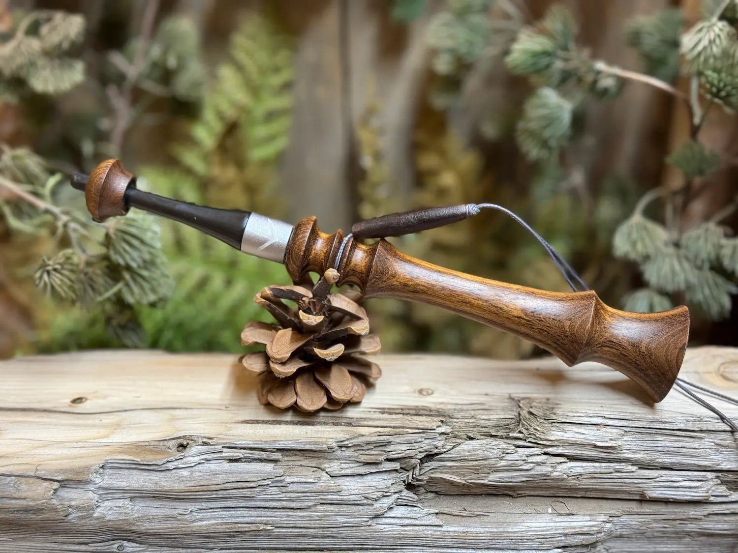 Brown Mora wood turkey trumpet with a lanyard and custom turkey print collar sitting on it's side balanced on a pine cone on a weathered wood platform.