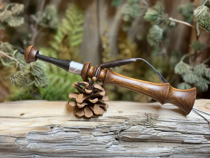 Brown Mora wood turkey trumpet with a lanyard and custom turkey print collar sitting on it's side balanced on a pine cone on a weathered wood platform.