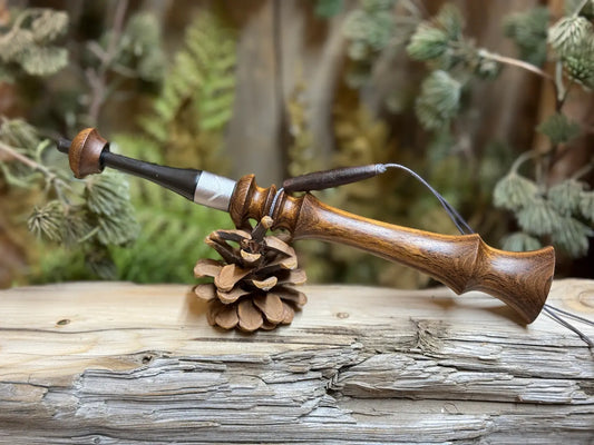 Brown Mora wood turkey trumpet with a lanyard and custom turkey print collar sitting on it's side balanced on a pine cone on a weathered wood platform.