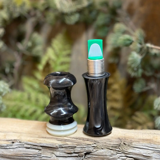 Short Reed Goose call sitting open with two parts, the thread-together design shows the short reed for the call inside the "guts" of the call. It's made with the signature swirling acrylic patterns of silver and brown like smoky on carbon. HD Carbon Acrylic from Deadshot Polymer's with white central faux ivory ring with built-in lanyard groove in the mouthpiece half.