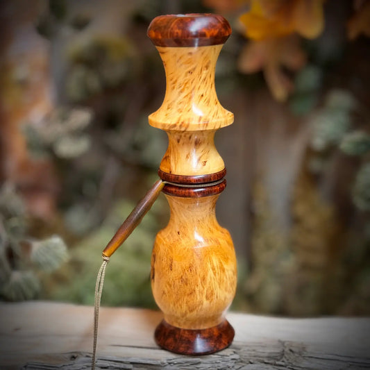 A large glowing blonde Yellow Cedar Burl Whitetail deer grunt with snakewood caps and accents sits polished with buffalo horn beaded lanyard upright and majestic on a piece of driftwood.